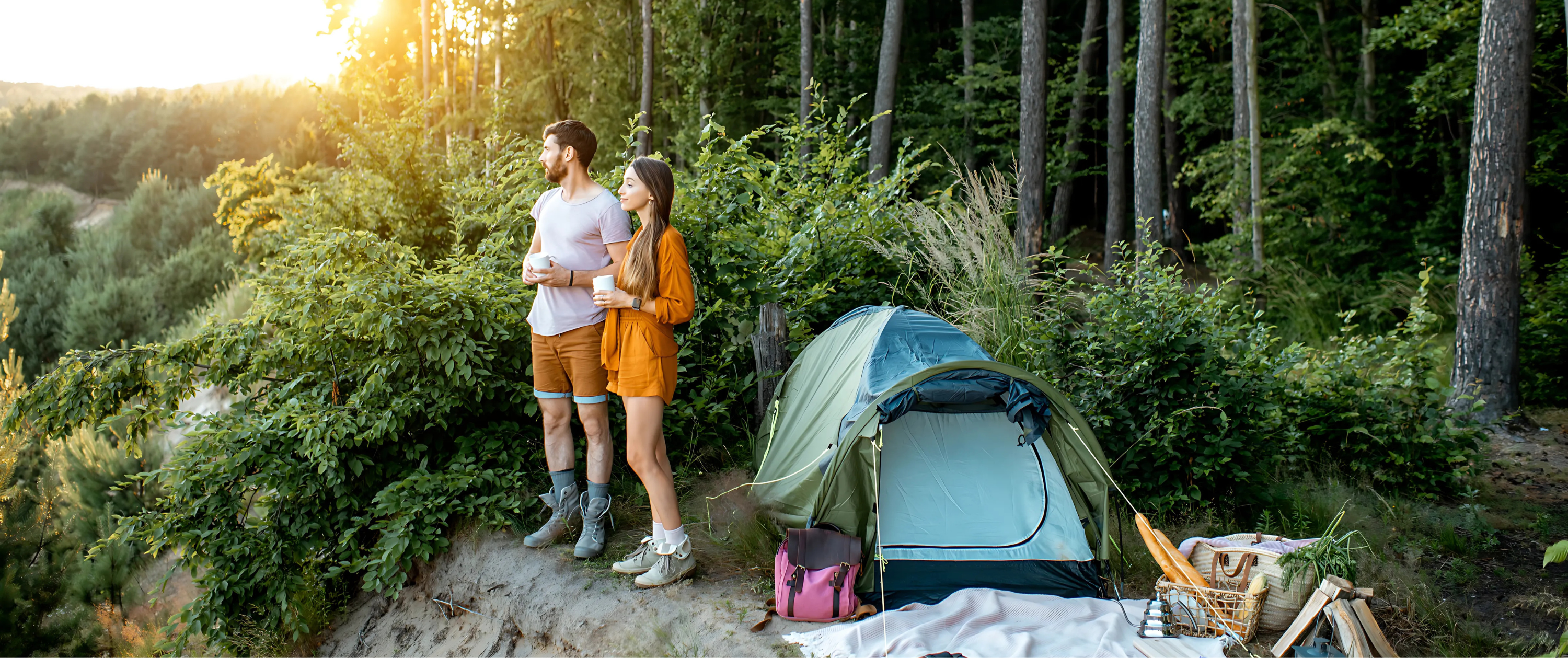 Couple standing next to a tent in a forest at sunset